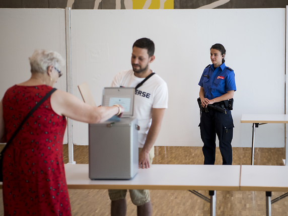 Une policière bernoise observe le bon déroulement du scrutin devant l'urne du bureau de vote installé à la Societ'halle ce dimanche à Moutier. © KEYSTONE/JEAN-CHRISTOPHE BOTT